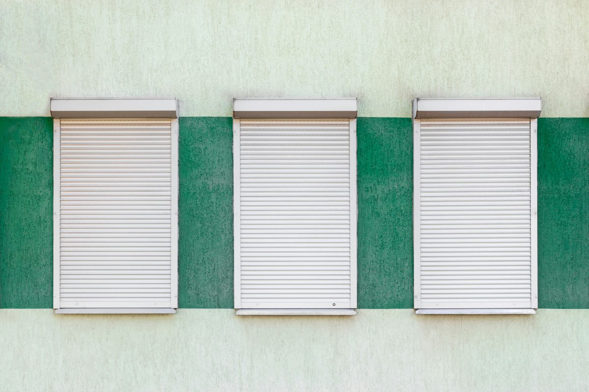 Closed roll-down shutters over three windows on a green and white wall